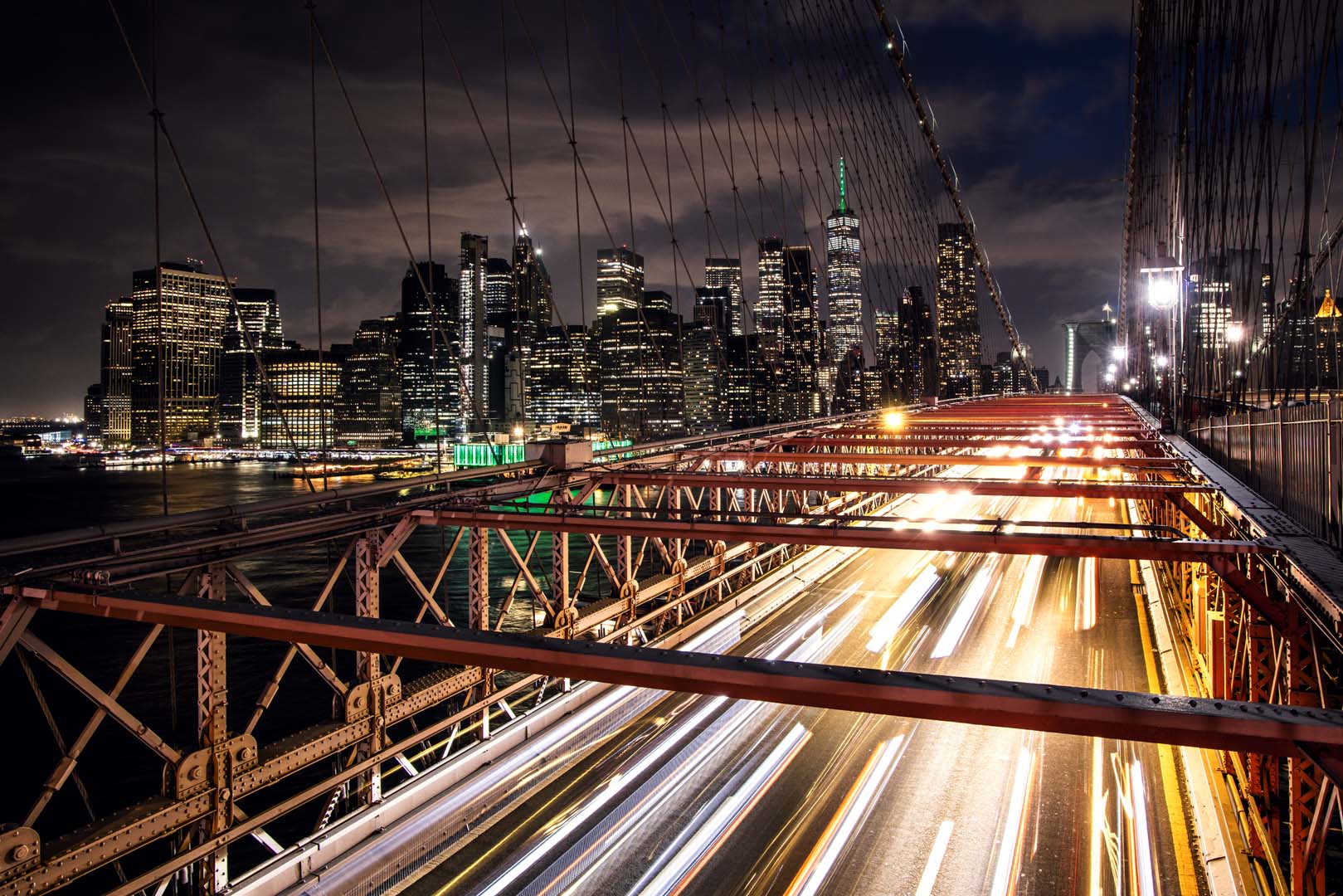 Brooklyn Bridge walkway at night with traffic light trails and the Manhattan skyline