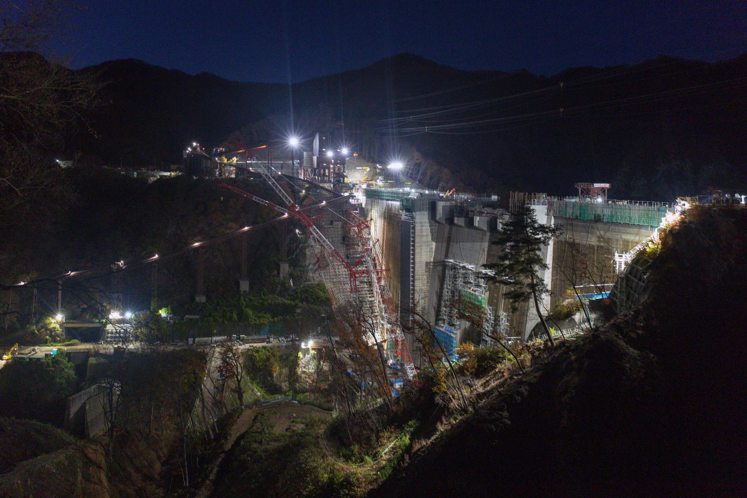Floodlit dam construction site in a night valley