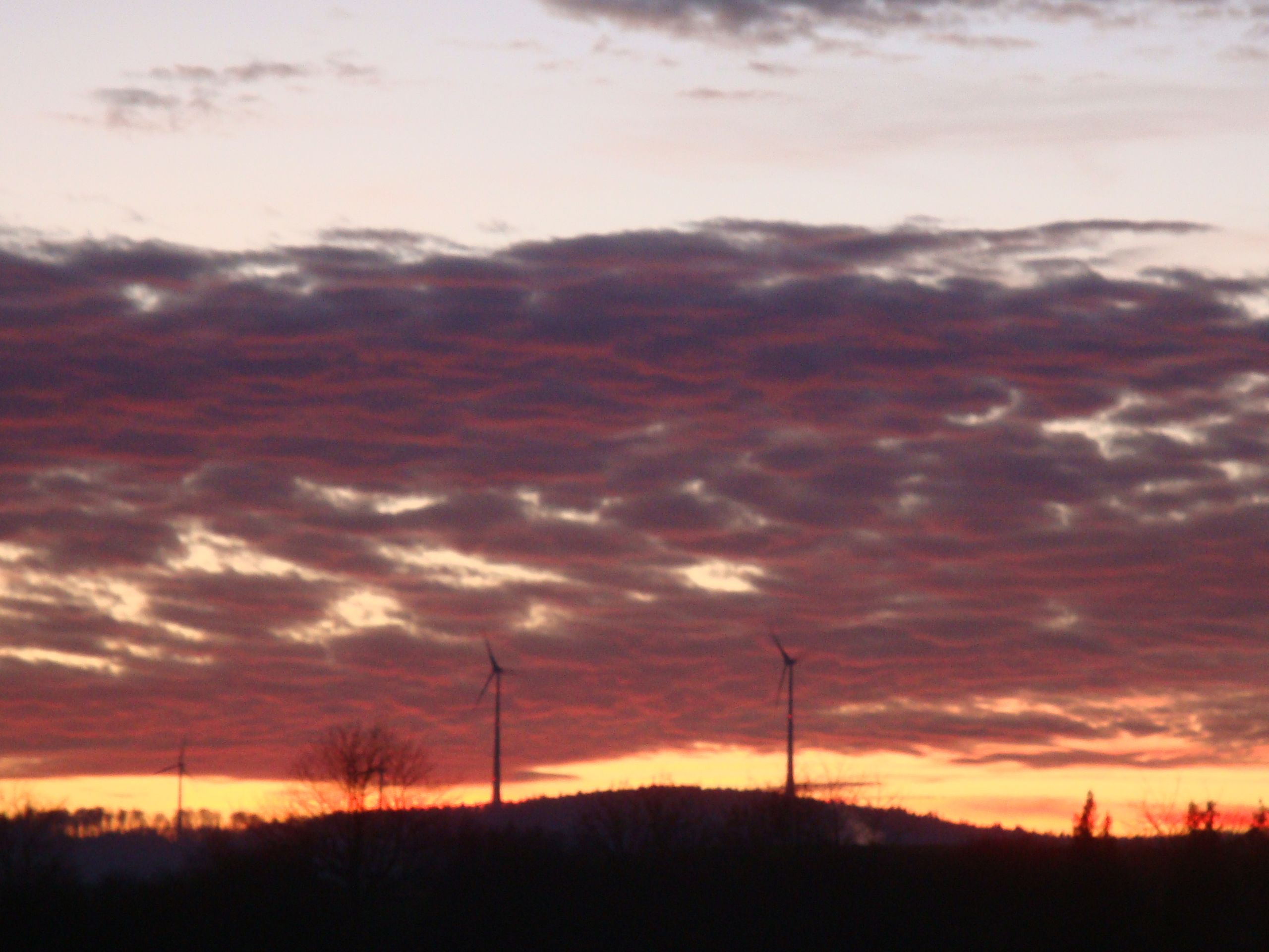 Wind turbines silhouetted under a blazing red-orange sunset